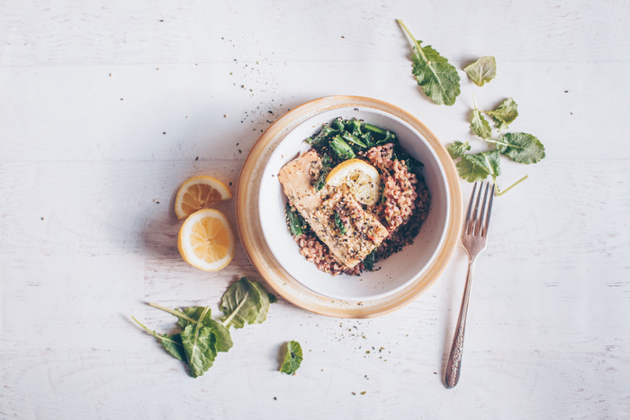 picture of a bowl with Mediterranean diet food including leafy greens, fish, whole grains, lemon, sesame seeds, and olive oil